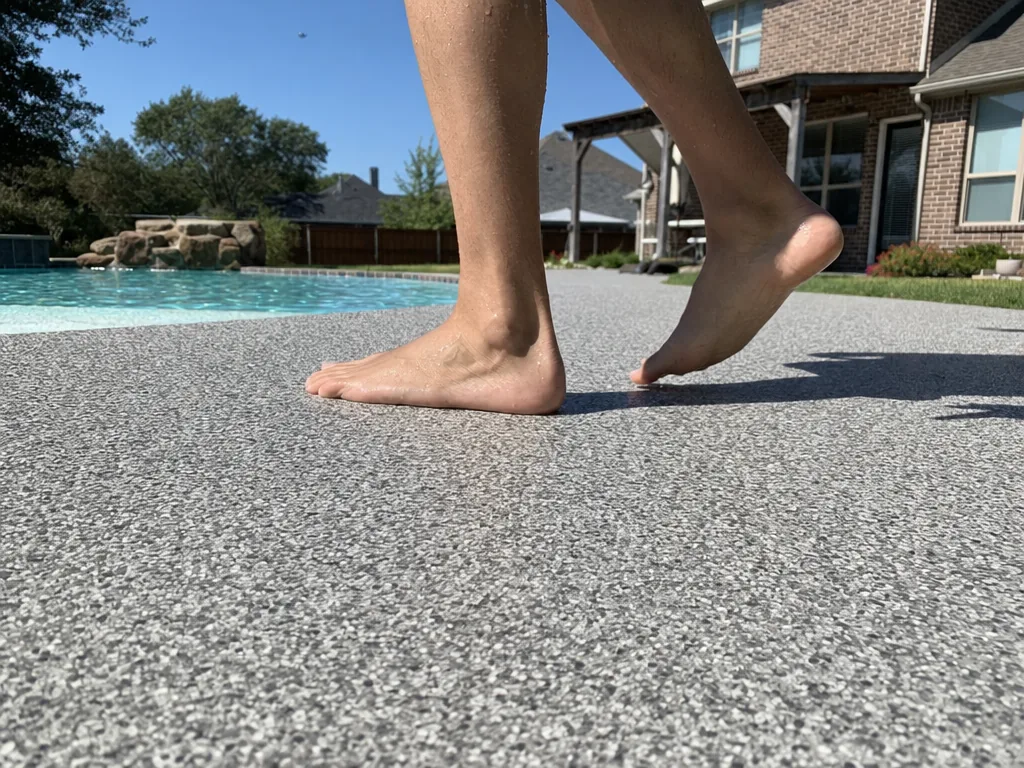 Bare feet walking on a light gray textured pool deck coating beside a pool